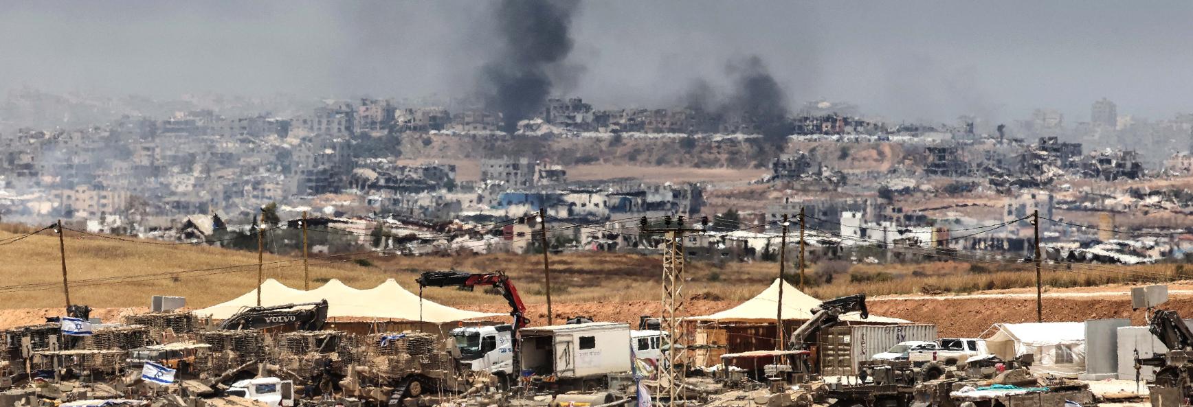 This picture taken from a position in southern Israel on the border with the Gaza Strip shows Israeli tanks and bulldozers deployed as smoke billows over destroyed buildings in Gaza during Israeli bombardment on May 17, 2025. 
