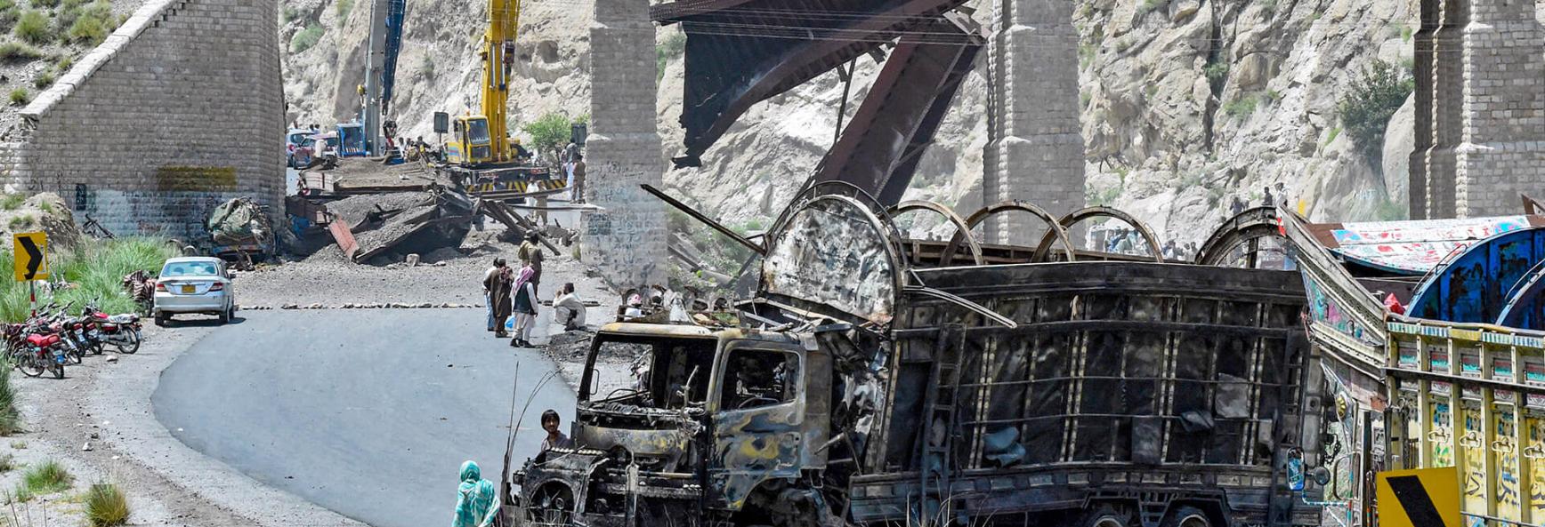 Residents stand beside a charred vehicle near a collapsed railway bridge the morning after a blast by separatist militants at Kolpur in Bolan district, Balochistan province on 27 August&nbsp;2024. 