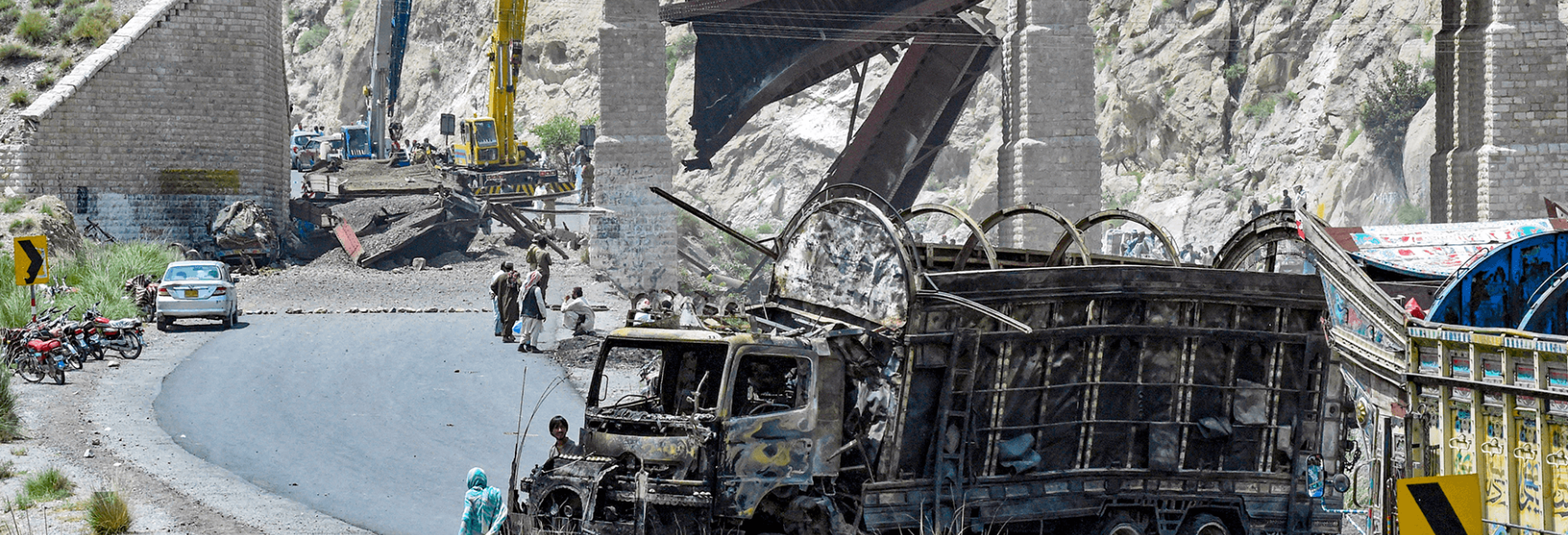 Residents stand beside a charred vehicle near a collapsed railway bridge the morning after a blast by separatist militants at Kolpur in Bolan district, Balochistan province, on 27 August 2024.