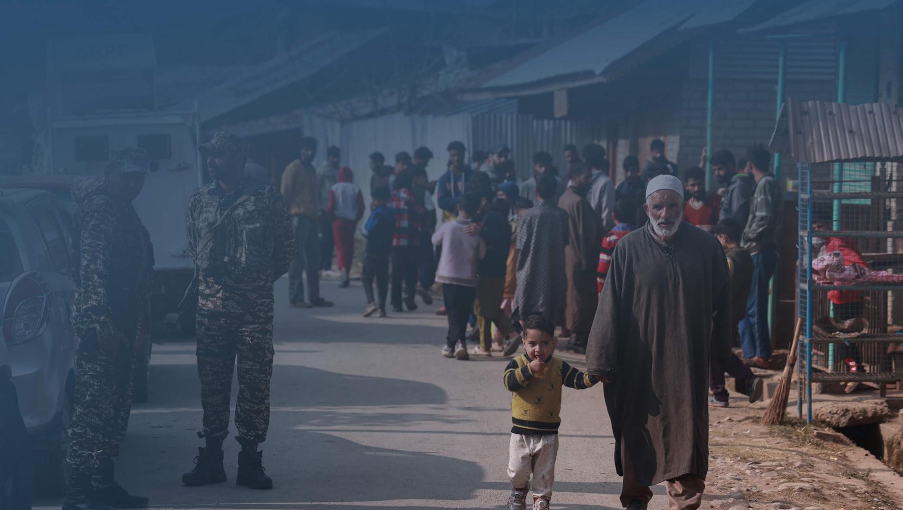 An elderly man walks while holding a child toward a site where two militants are killed in Sopore, Jammu and Kashmir, India, on 8 November 2024.