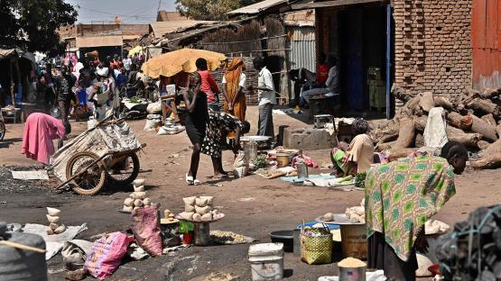 A photo of a man hacking at logs with an axe as people walk past at an open market in Wau on February 2, 2020.