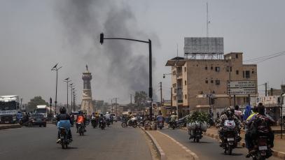 Black smoke rises above buildings as traffic passes the Africa Tower monument in Bamako on 26 April 2026, when rebels from the Azawad Liberation Front (FLA) coalition and militants from Jama&rsquo;at Nusrat al-Islam wal-Muslimin (JNIM) targeted several areas in the country. 