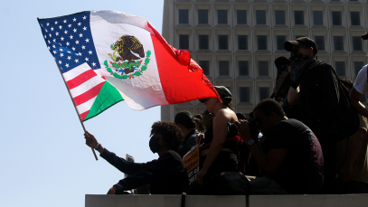 A demonstrator waves a combination Mexican-American flag during a protest against ICE raids and the deployment of the National Guard at The Federal Building in Downtown Los Angeles on June 9, 2025.